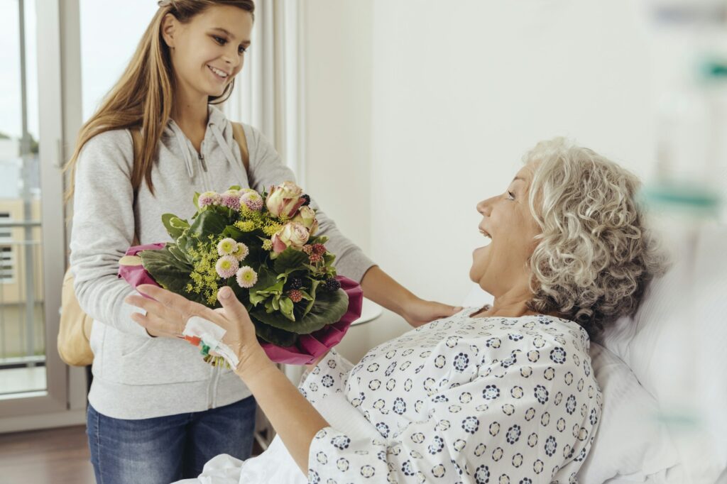 Granddaughter visiting grandmother in hospital, bringing bunch of flowers